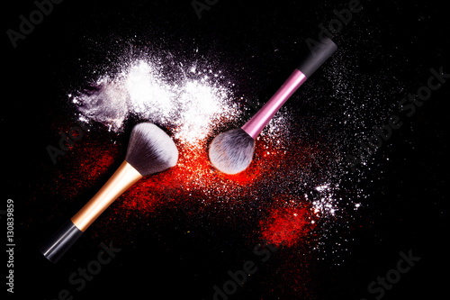 Make-up brushes with colorful powder on black background. Explosion stars dust with bright colors. White and red powder.