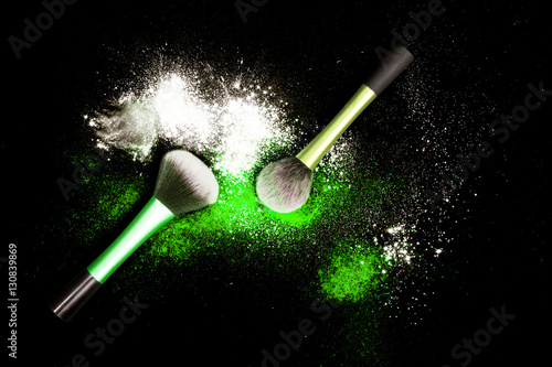 Make-up brushes with colorful powder on black background. Explosion stars dust with bright colors. White and green powder.