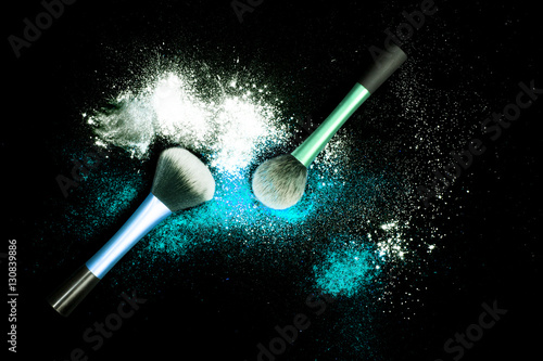 Make-up brushes with colorful powder on black background. Explosion stars dust with bright colors. White and turquoise powder.