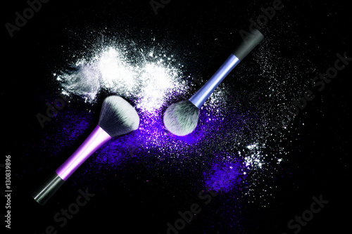 Make-up brushes with colorful powder on black background. Explosion stars dust with bright colors. White and blue powder.