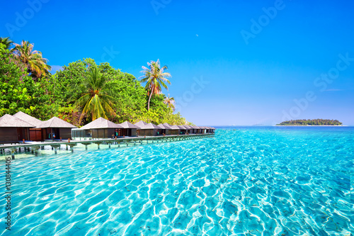 Overwater bungalows on tropical island with sandy beach, palm trees and beautiful lagoon