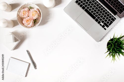 Stylish minimalistic workplace with laptop keyboard, vintage tray with roses, office plant, notebook, sunglasses in flat lay style. White background. Top view.