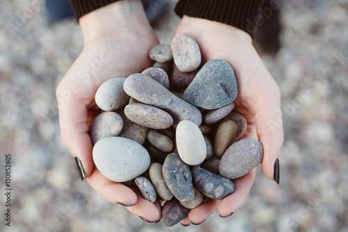 Woman holding smooth pebbles on rocky beach