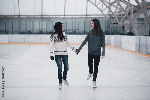Friends on skates at ice-skating rink skating together.