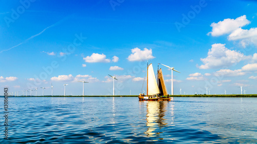 Two Historic Wooden Botter Boats in Full Sail near a Wind Farm along the Shore of Veluwemeer in the Netherlands photo