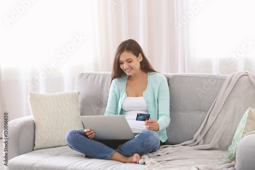 Young woman sitting on sofa and making online shopping