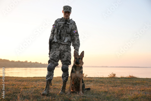 Soldier with german shepherd dog near river at sunset