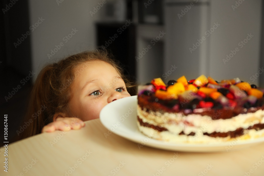Cute little girl going to taste sweet cake left on kitchen table