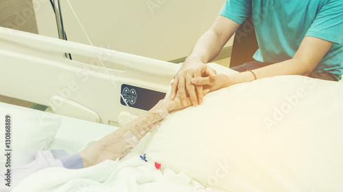 Son holding mother's hand , giving her his support after having surgery 
