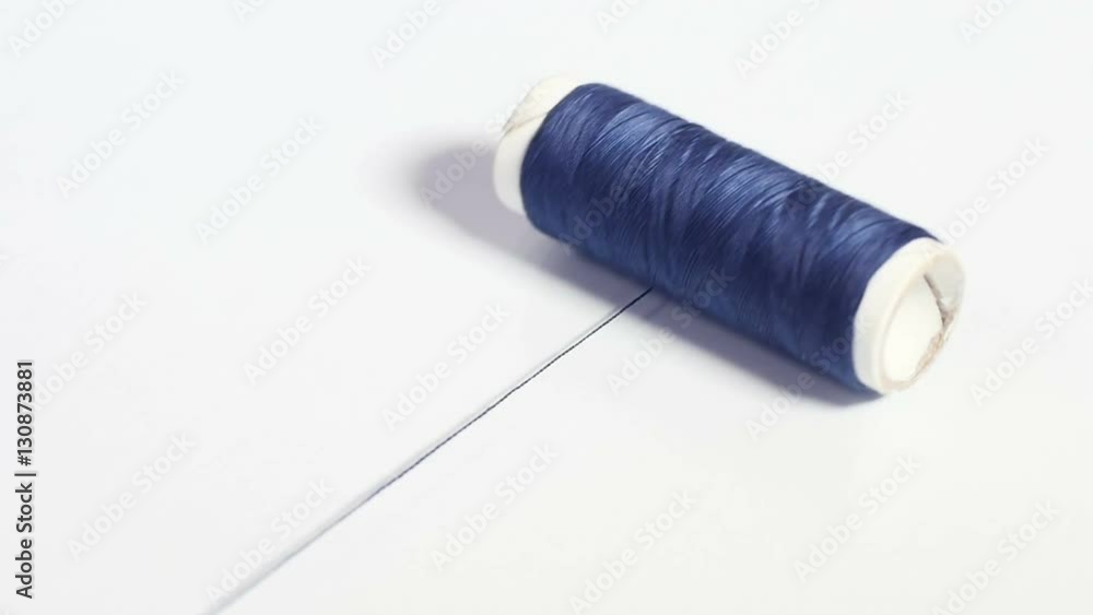 Isolated spool of dark blue thread rolling on white surface, white paper bobbin, sewing accessories, tools for tailoring, haberdashery. Close up, shallow DOF, 4K Ultra HD. Isolated spool of dark blue thread rolling on white surface, white paper bobbin, sewing accessories, tools for tailoring, haberdashery. Close up, shallow DOF, 4K Ultra HD.