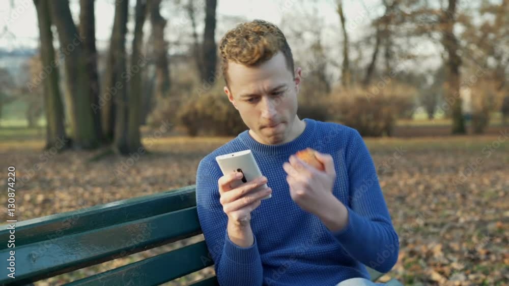 Man eating apple and texting on smartphone in the autumnal park, steadycam shot
Man eating apple and texting on smartphone in the autumnal park, steadycam shot