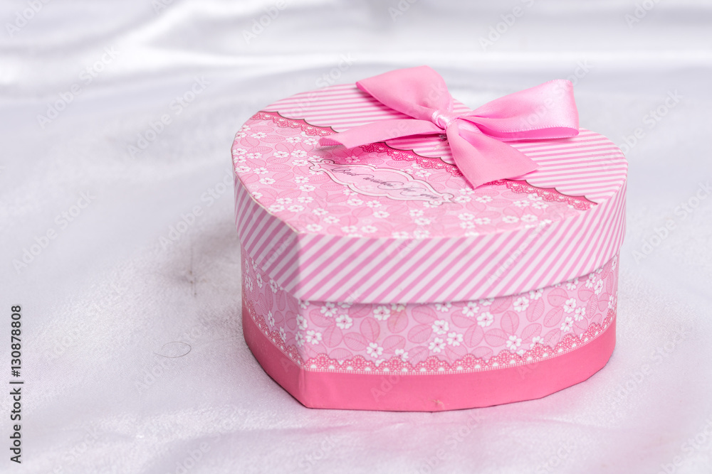 Pink heart shaped gift box with bow over white satin Pink heart shaped gift box with bow over white satin
