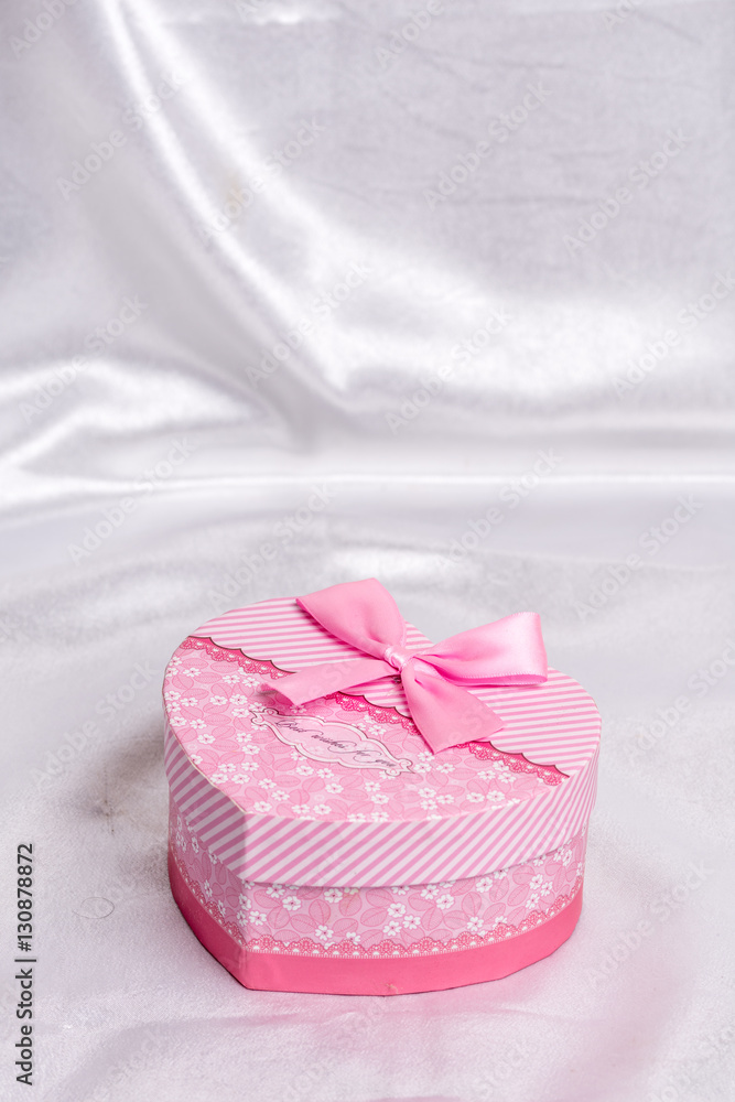 Pink heart shaped gift box with bow over white satin Pink heart shaped gift box with bow over white satin