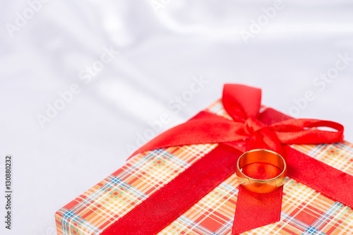 Gift box with wedding ring on it over white satin