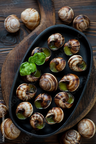 Frying pan with escargot snails on a rustic wooden background