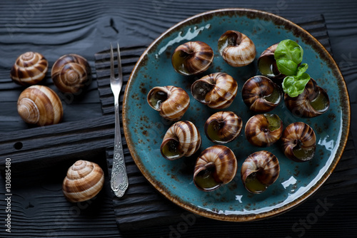 Baked snails with garlic herbs butter on a black serving board