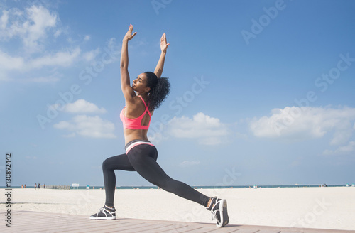 Mixed race girl exercising in a lunge with arms up on beach