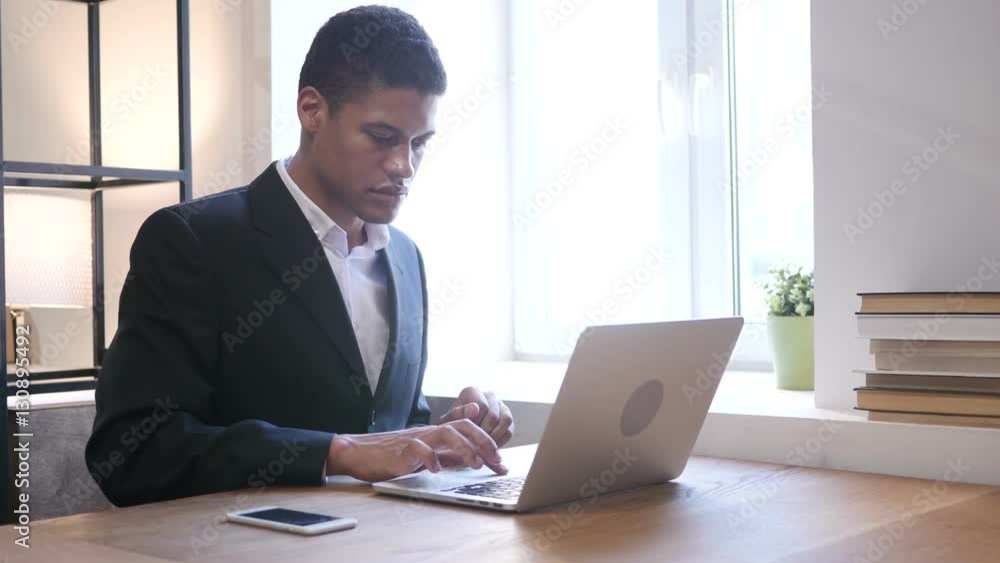 Black Businessman Upset by Loss while Working on Laptop Black Businessman Upset by Loss while Working on Laptop