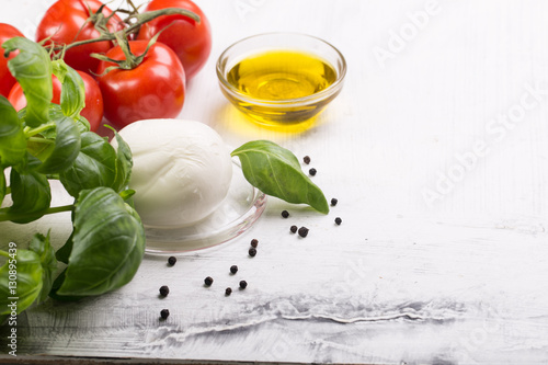 Ingredients for cooking italian capreze salad cherry tomatoes, basil leaves, mozzarella cheese, spices and olive oil on wooden rustic background top view close up photo