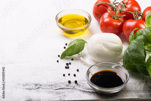 Ingredients for cooking italian capreze salad cherry tomatoes, basil leaves, mozzarella cheese, spices and olive oil on wooden rustic background top view close up