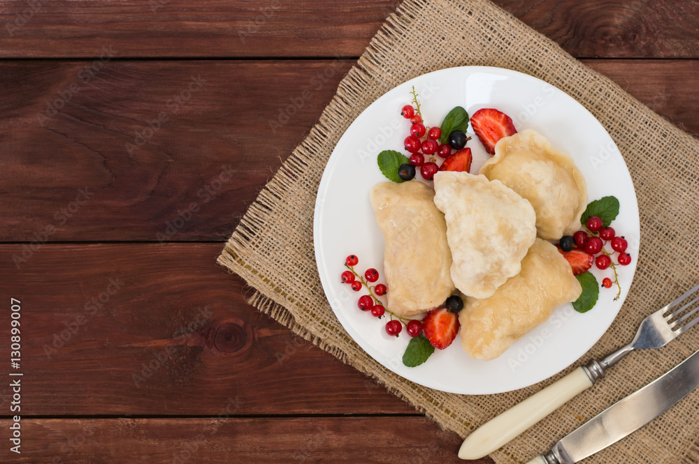 Dumplings with strawberries on a background of wild berries. Wooden rustic table. Top view. Close-up Dumplings with strawberries on a background of wild berries. Wooden rustic table. Top view. Close-up