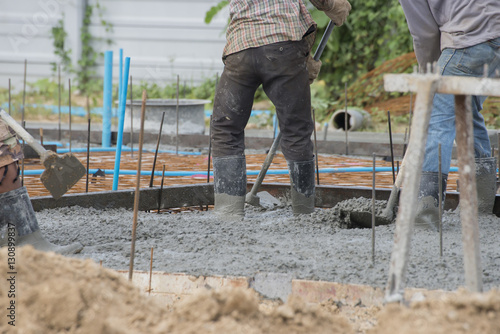 Concrete casting work.Worker wearing blue jeans and plastic brown boots leveling concrete work step of the building construction.