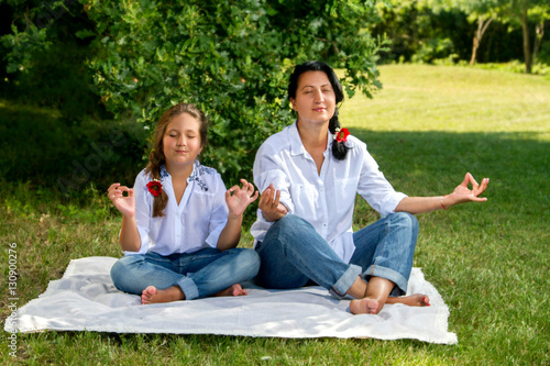 Mother and daughter meditating sitting on the grass