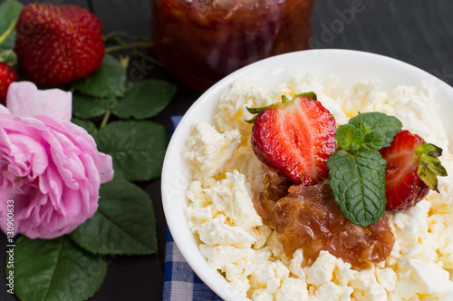 Cottage cheese and jam of roses with a strawberry. Wooden black table. Top view. Close-up