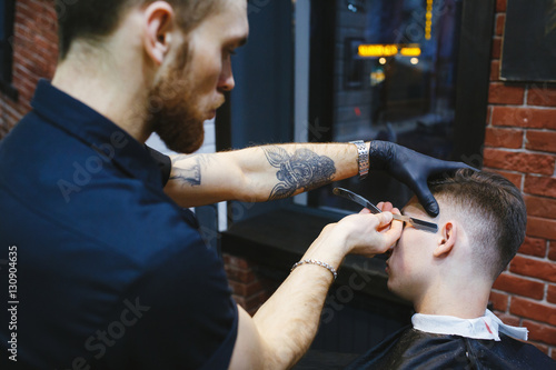 Hairdresser shaving man with a straight razor