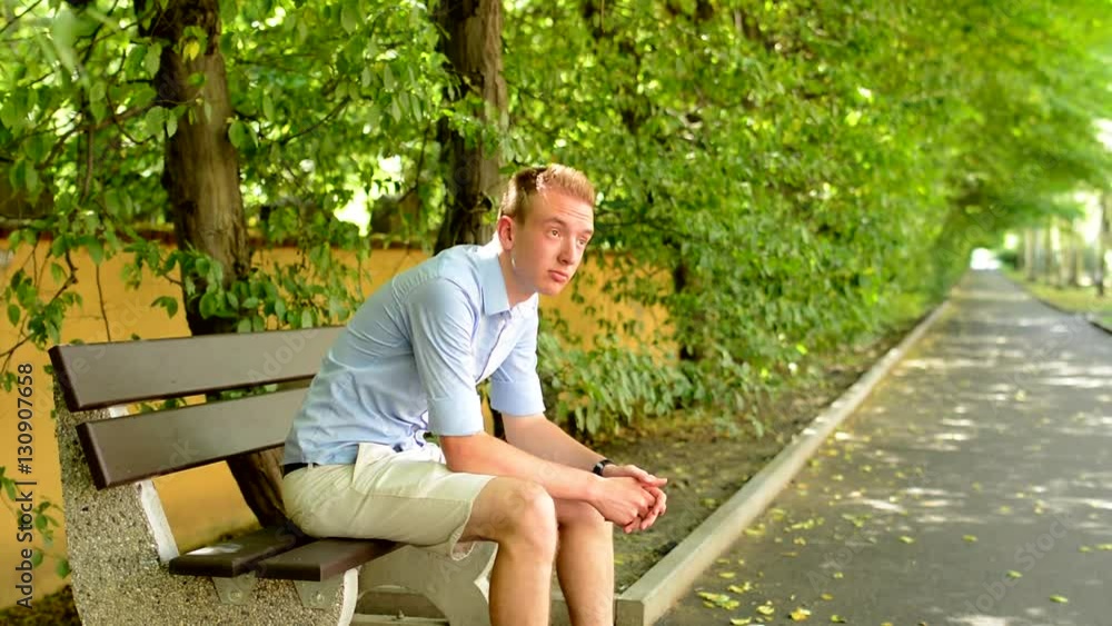 young handsome patient man sits on the bench in the park - he look around young handsome patient man sits on the bench in the park - he look around