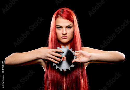 Portrait of beautiful girl with circular saw blade. Bretty naked woman, long red hair,  nude body, sawblade, dark background. Female and sharp stainless steel disc photo