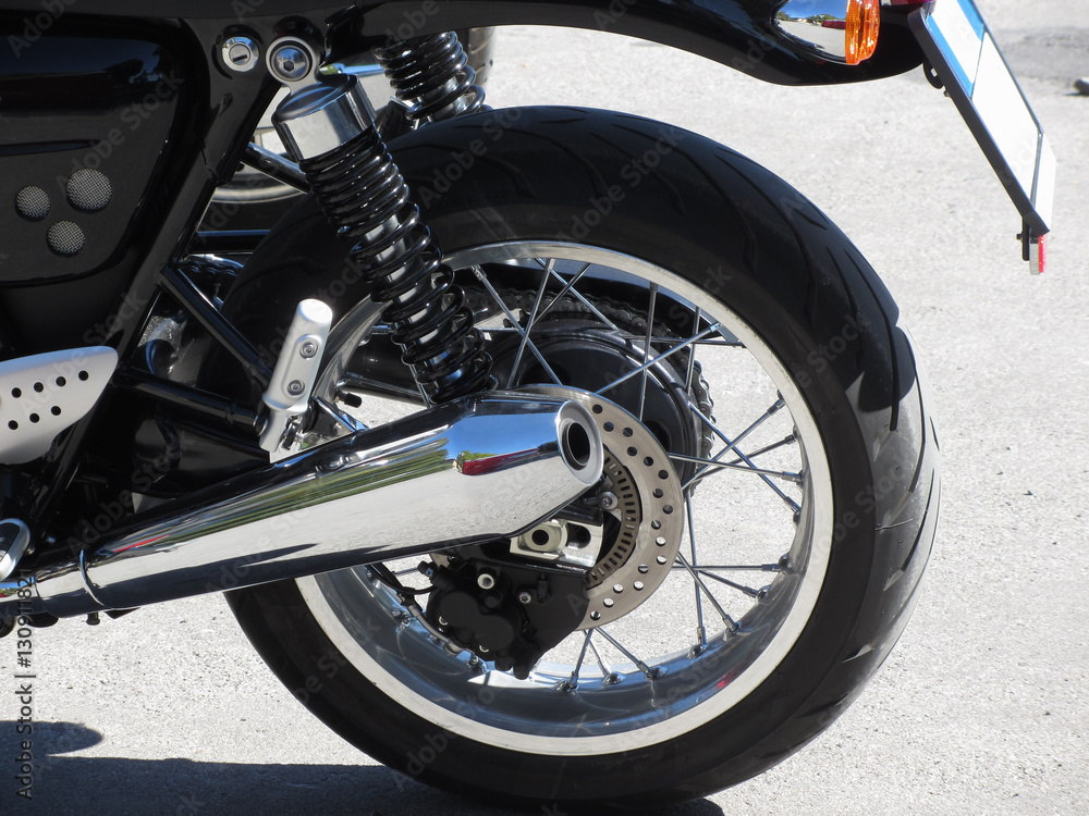 Rear wheel and chromed exhaust pipe of a classic motorcycle . Side view