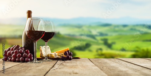 Murais de parede Red wine served on wooden planks, vineyard on background