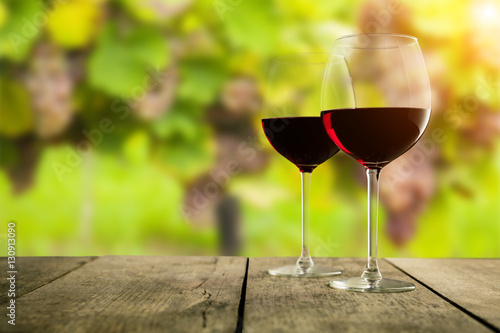 Red wine glasses served on wooden planks, vineyard on background