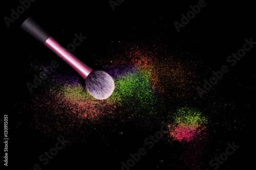 Colorful makeup powder on black background with pink brush.