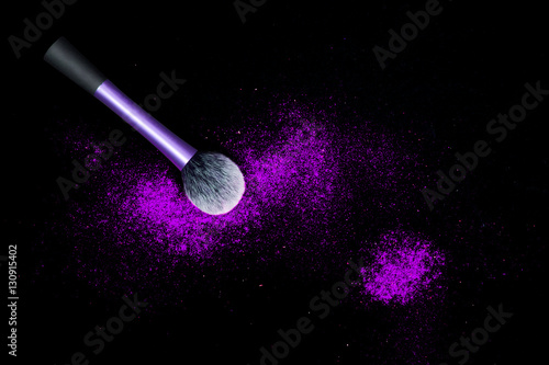 Make-up brush with colorful powder spilled glitter dust on black background. Makeup brush with bright colors. Purple powder on black table.