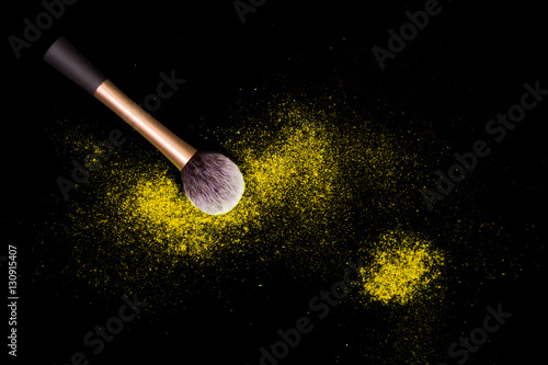 Make-up brush with colorful powder spilled glitter dust on black background. Makeup brush with bright colors. Yellow powder on black table.