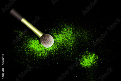 Make-up brush with colorful powder spilled glitter dust on black background. Makeup brush with bright colors. Green powder on black table.