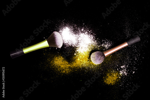 Make-up brushes with colorful powder spilled glitter dust on black background. Makeup brush on new year's Party with bright colors. White and yellow powder.