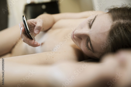 junge Frau liegt nackt auf dem Bett mit einem Smartphone