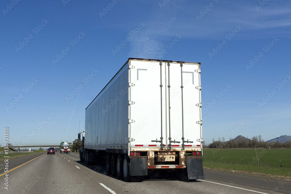 Rear view of white semi on interstate under blue sky.