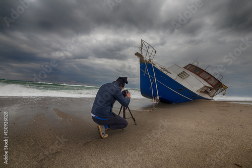 Uomo fotografo di fronte a una barca di immigrati clandestini arenata sulla spiaggia. Fotografie estreme concetto. photo