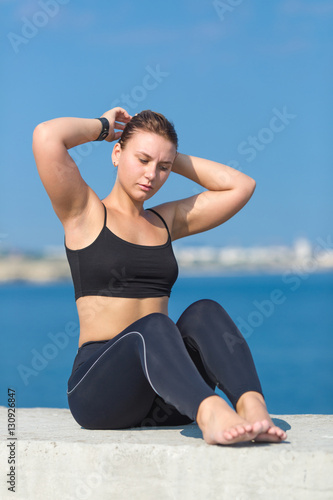 Young sportswoman sits on concrete and adjusts her hairstyle