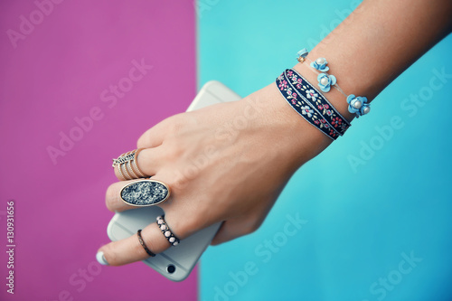 Female hand with jewelry and cellphone on color background