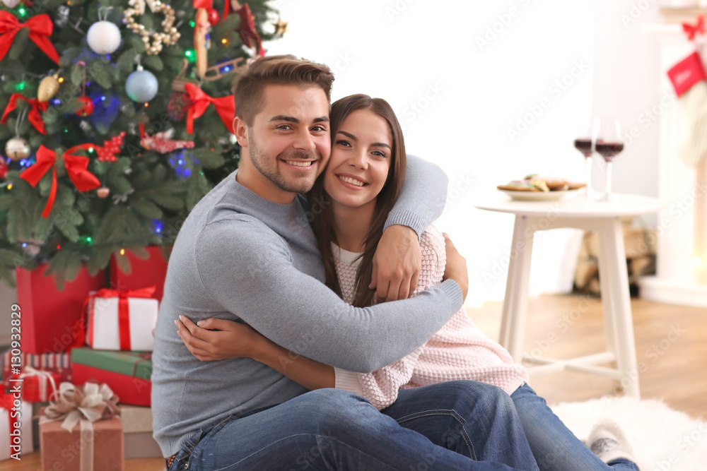 Young couple near Christmas tree indoors