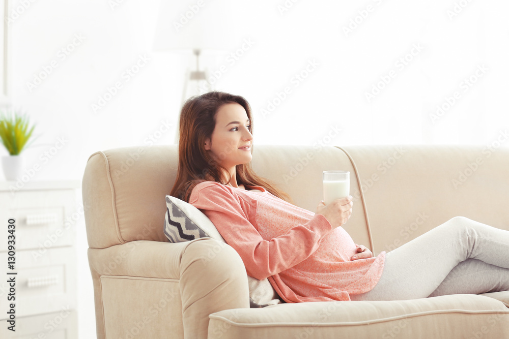 Young pregnant woman with glass of milk sitting on sofa in the room Young pregnant woman with glass of milk sitting on sofa in the room