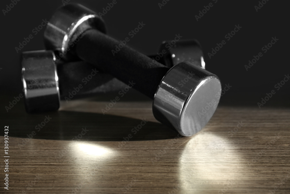 Dumbbells on wooden surface against dark background Dumbbells on wooden surface against dark background
