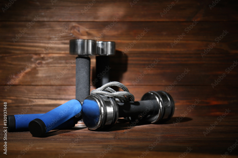 Dumbbells and skipping rope on wooden background Dumbbells and skipping rope on wooden background