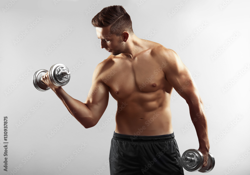 Sporty man doing exercises with dumbbells on light background