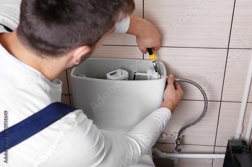 Plumber repairing toilet cistern at water closet photo